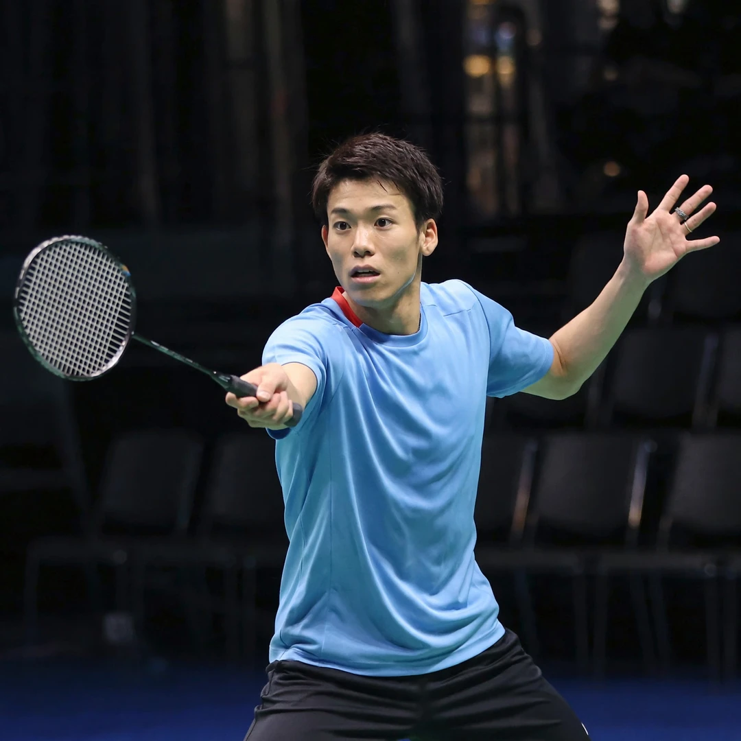 Riki Takei playing a backhand during an international men's singles match Riki Takei playing a backhand shot deep in the rear court, racket in his right hand (AI-generated)